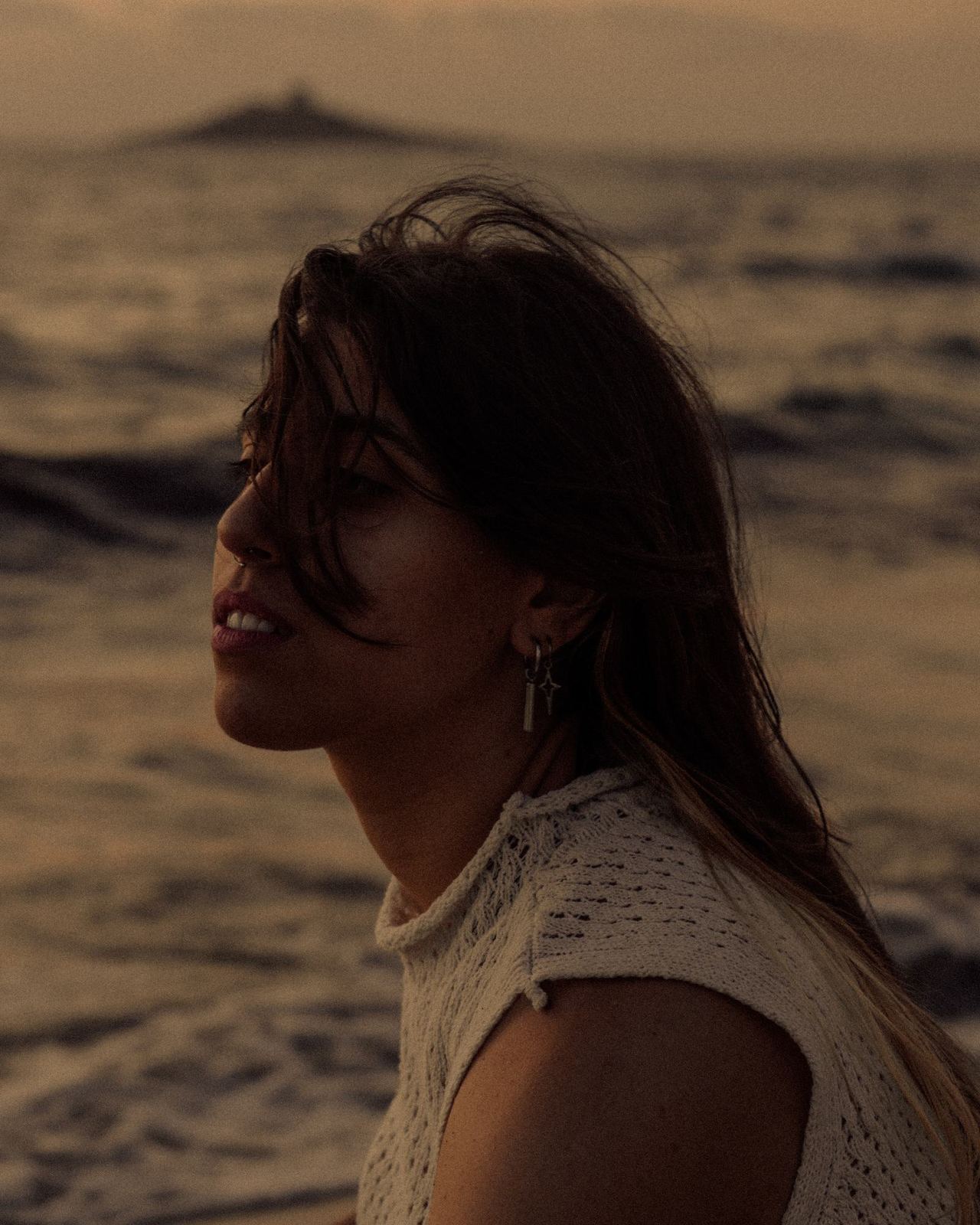 Ritratto di donna con i capelli mossi dal vento, luce calda di fine giornata sulla spiaggia