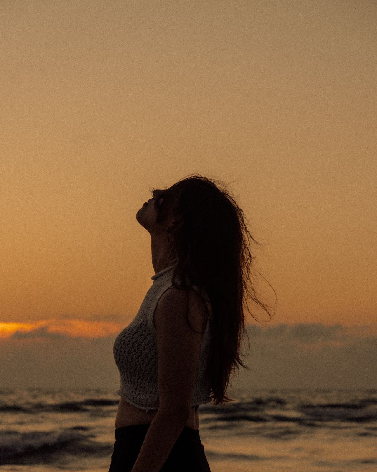 Silhouette di donna in piedi davanti al mare al tramonto