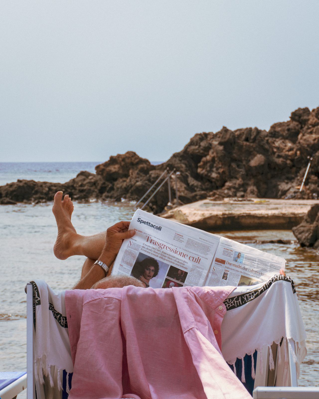 Dettaglio di piedi e giornale su un telo rosa in spiaggia