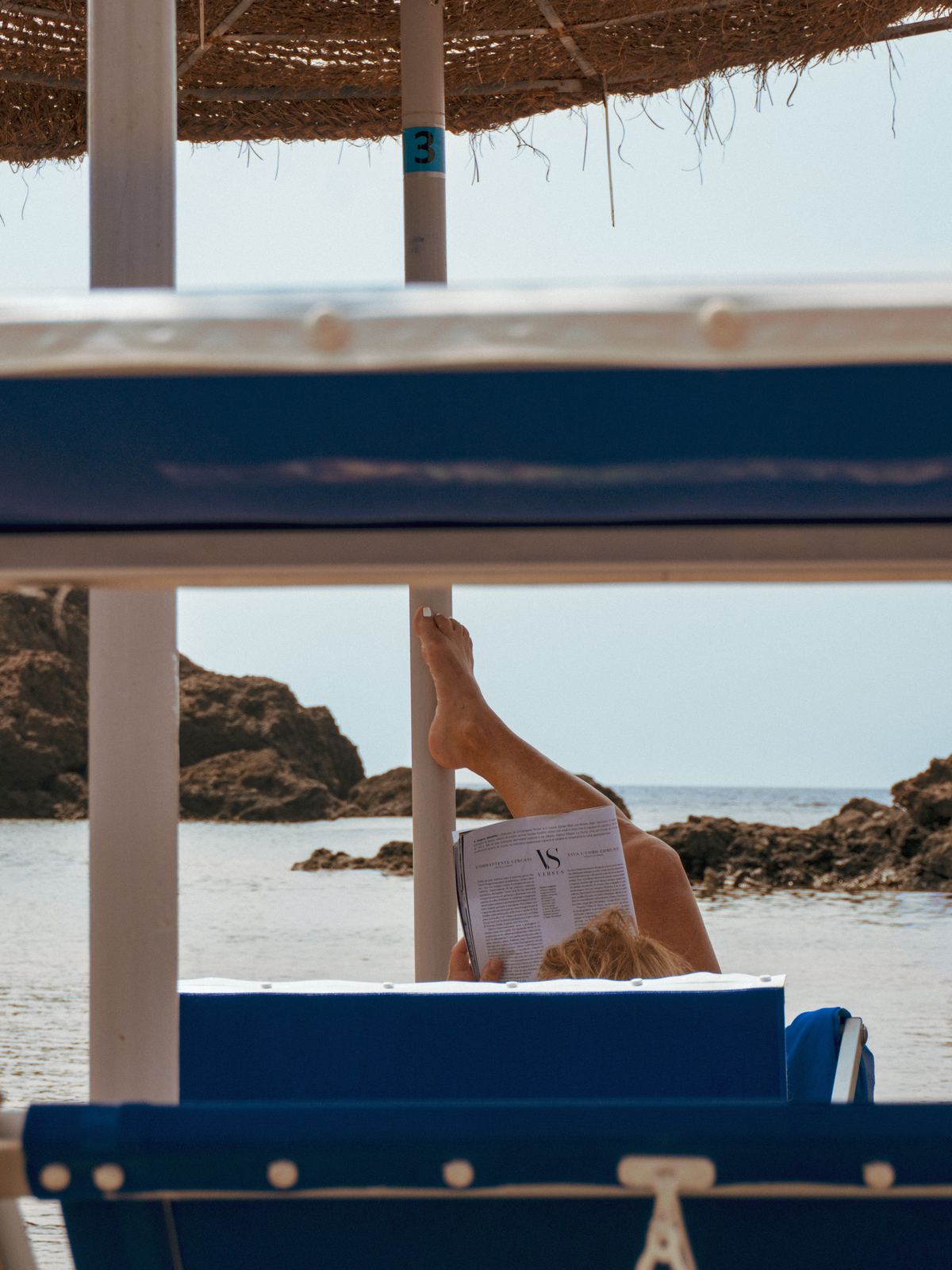 Lettini blu vuoti davanti al mare, vista fra i pali dell'ombrellone
