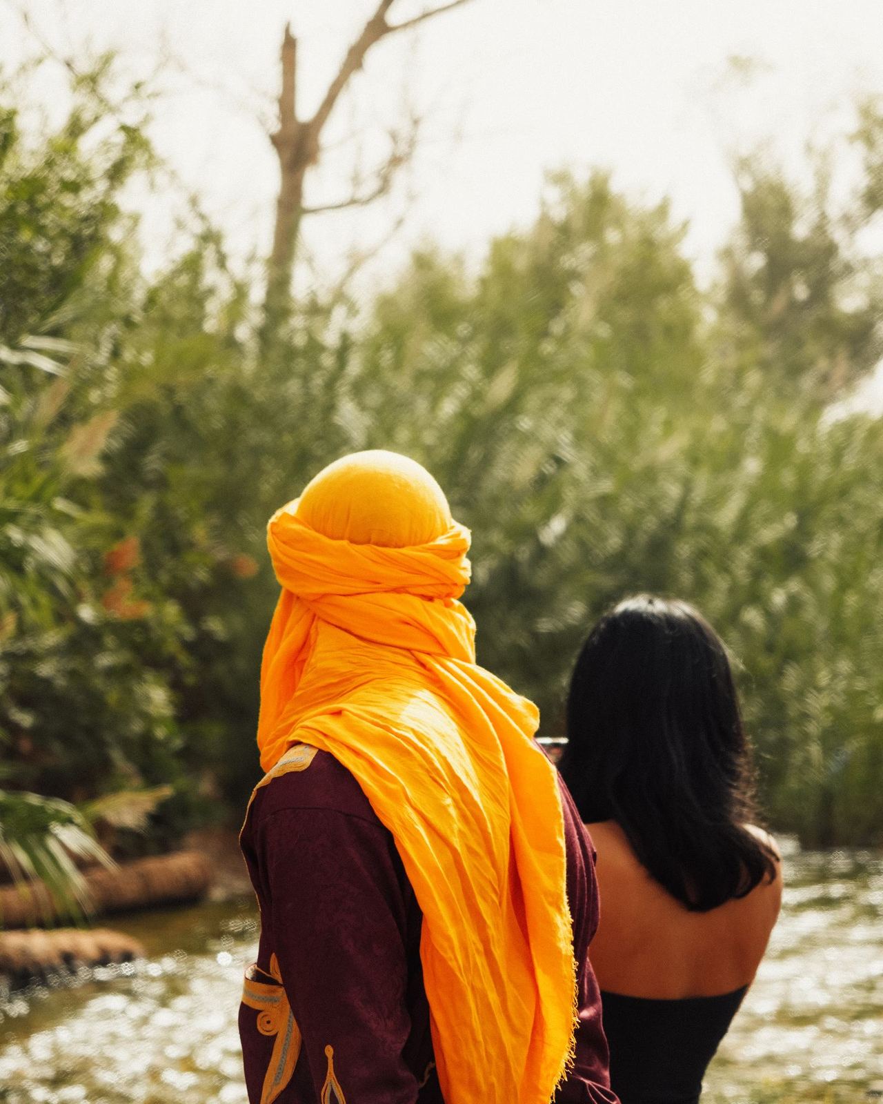 Uomo con turbante arancione di spalle, fra la vegetazione