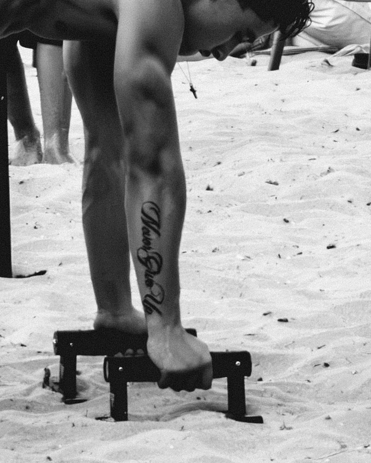Dettaglio di gambe sulla sabbia con tatuaggio, bianco e nero