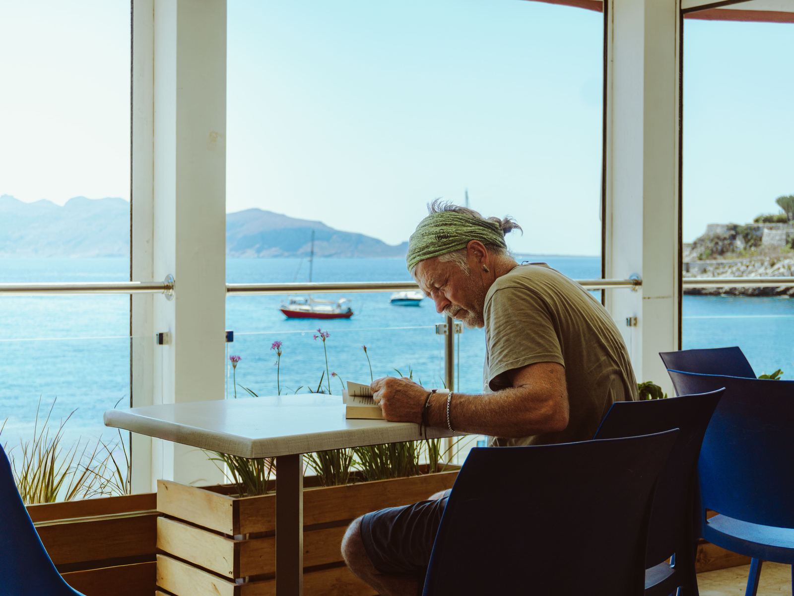 Uomo seduto al tavolo di un bar sul mare, vista sulla baia